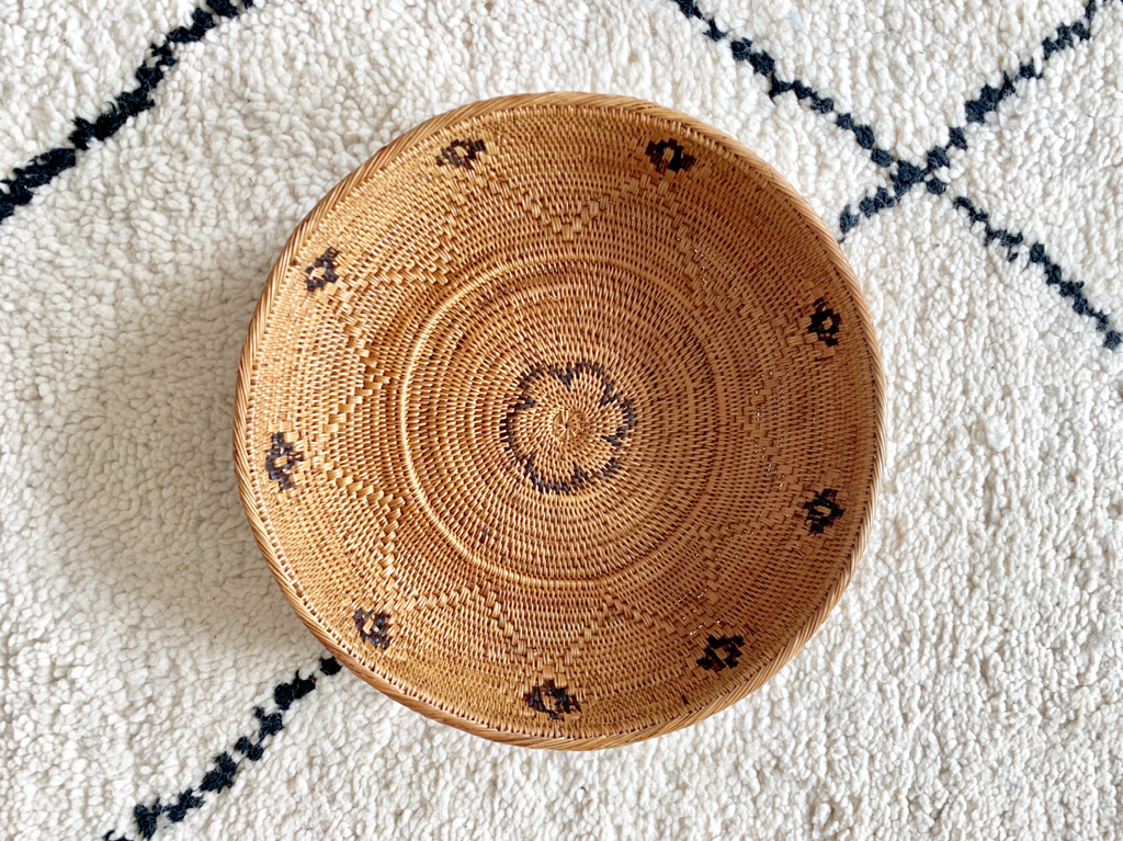 Black and natural woven Tenganan basket with intricate patterns on a textured white and black rug