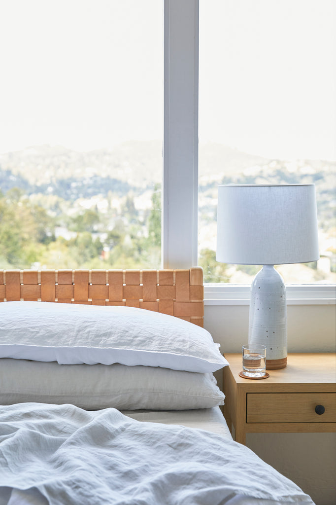 Styled Natural Linen Sheet Set with a Woven Leather Strap Headboard and an Oak and Leather Strap Side Table and a Hand Thrown Ceramic Lamp. - Saffron and Poe