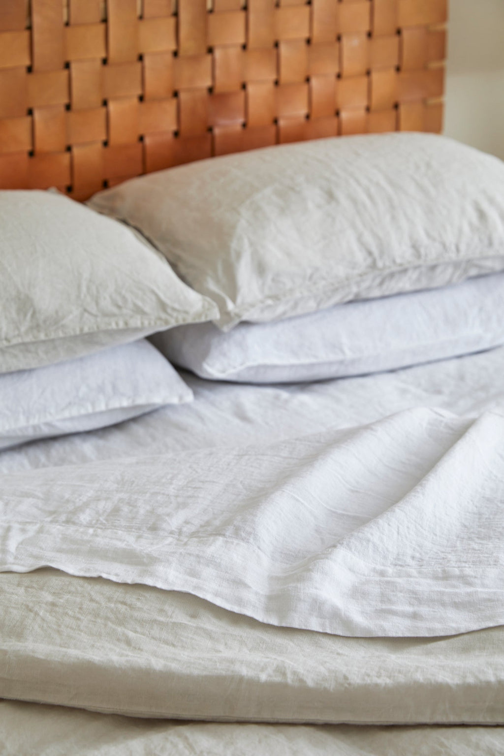 White linen sheet set with pillows on bed featuring soft, textured fabric and woven headboard