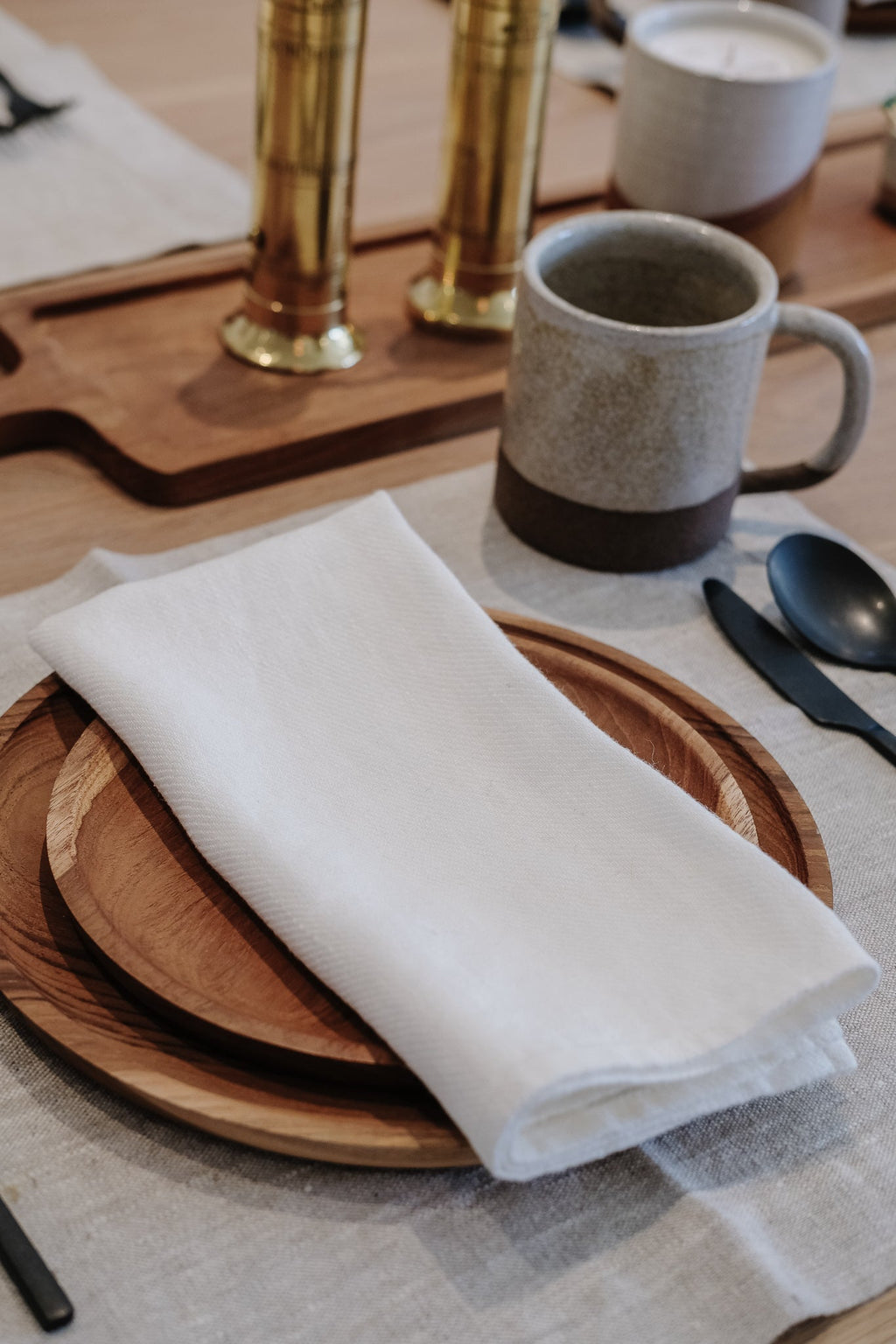 Hand-carved teak plate with white napkin on a dining table set with rustic mug, cutlery, and candles