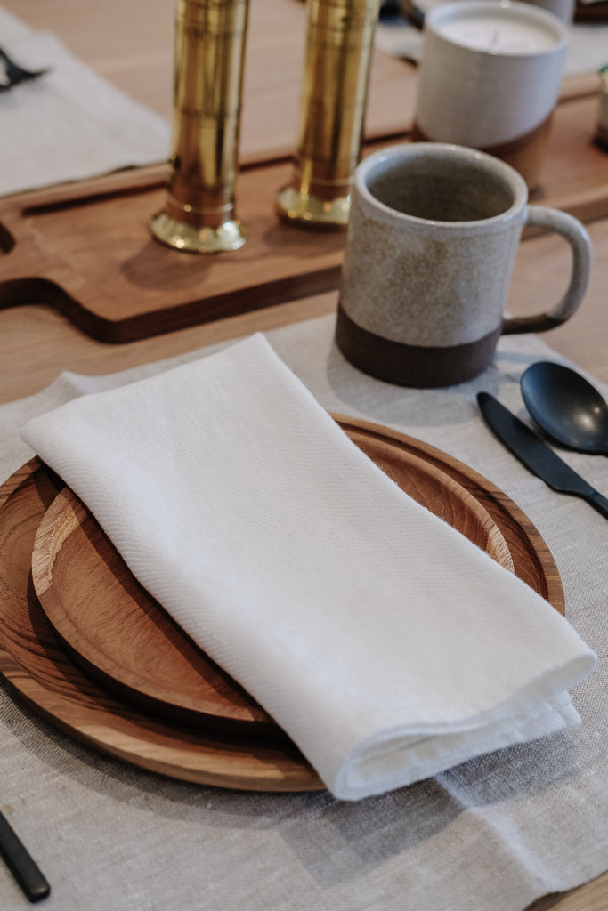 Close up of teak small plate and teak large plate on linen placemat with ivory linen napkin. - Saffron and Poe.