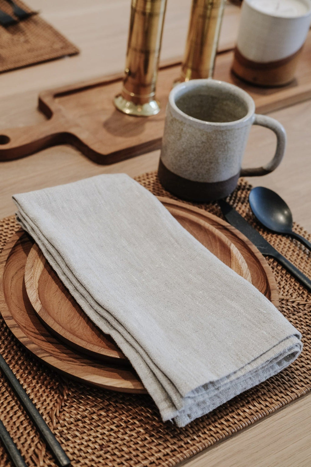 Natural linen napkin folded on wooden plate with ceramic mug and cutlery on woven placemat