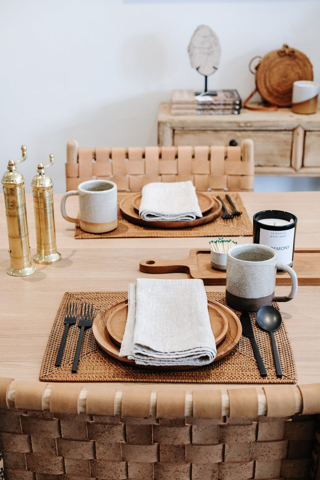 Woven Tenganan placemats on wooden dining table with plates, napkins, mugs, and cutlery in cozy rustic setting