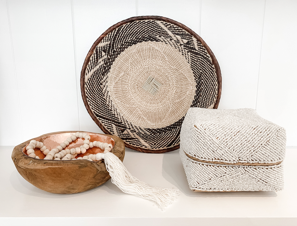 Saffron + Poe Curated Shelf Bundle with hammered copper and teak bowl, hand beaded Bali basket, tasseled Bali beads, and Ilala palm wall basket displayed on a white shelf