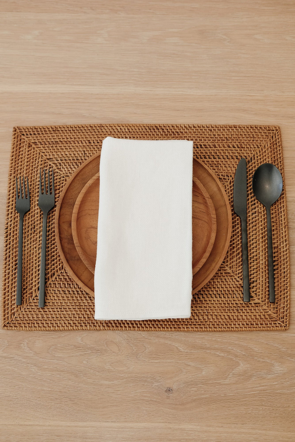 Ivory European linen napkin on wooden plate with woven placemat and black cutlery set