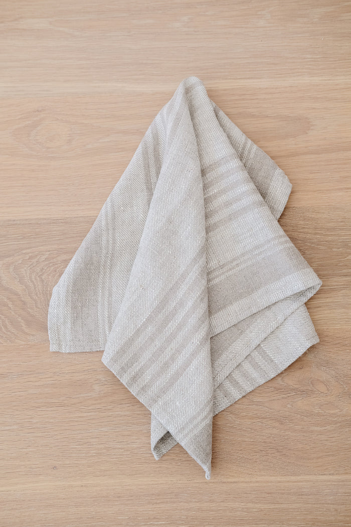 Top down view of draped Natural Stripe Linen Hand Towel (Set of 2) on a White Oak Dining Table. - Saffron and Poe