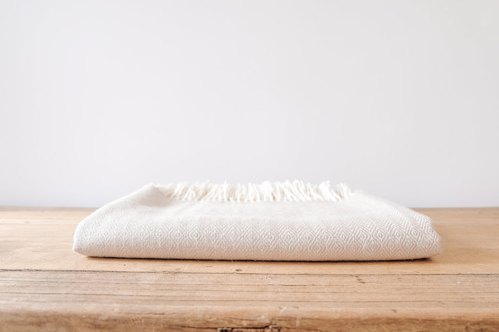 Beige baby alpaca throw blanket folded on wooden surface with fringe edges and subtle geometric pattern