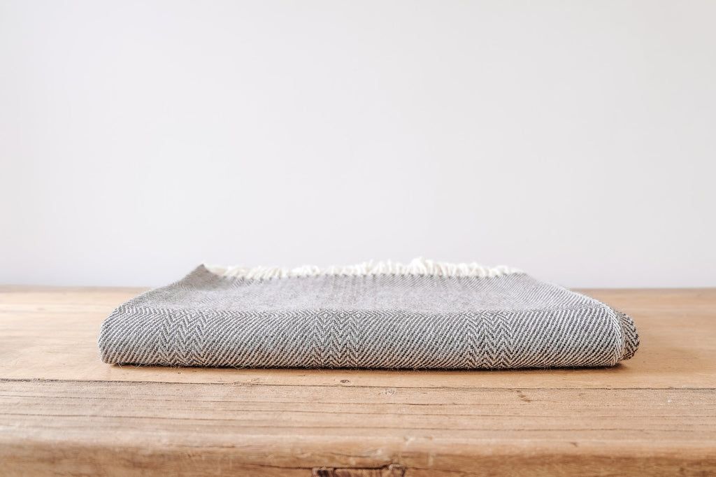 Folded charcoal brown baby alpaca throw blanket with geometric pattern on wooden surface