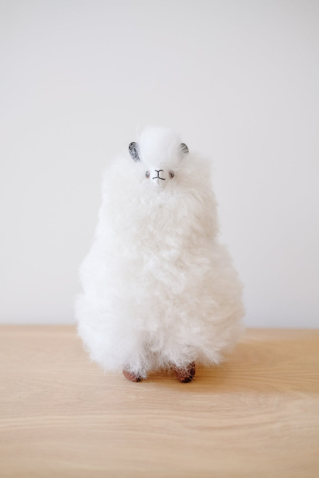 White fluffy Alpaquita stuffed animal made from baby alpaca wool standing on a wooden surface.