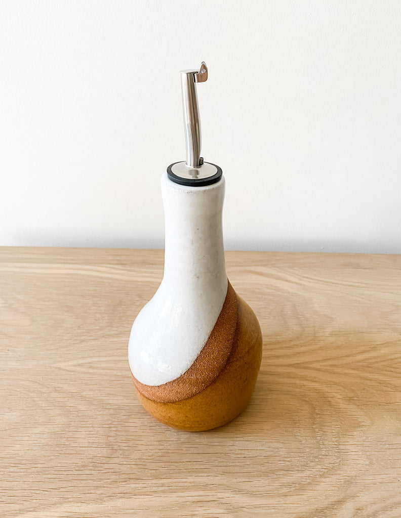 Front slightly tilted view of Uzumati Ceramic Olive Oil Bottle on white oak against a white wall - Saffron and Poe