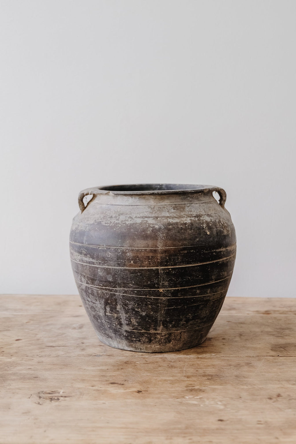Antique clay pot with rustic patina on wooden surface against white background