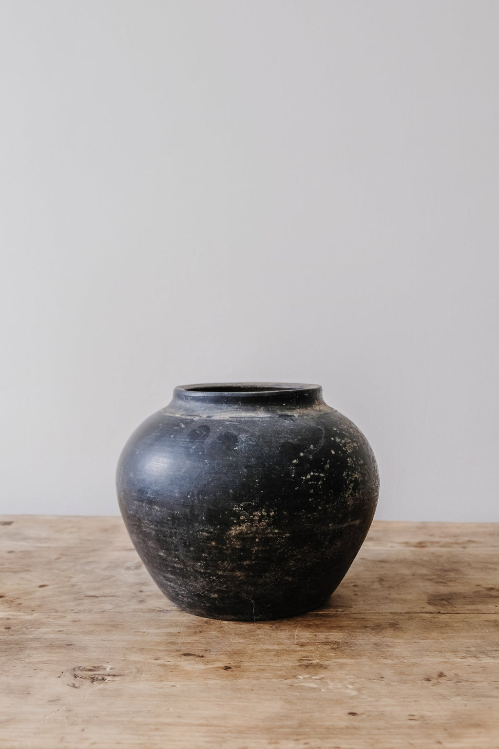Antique black clay pot on wooden surface with rustic patina