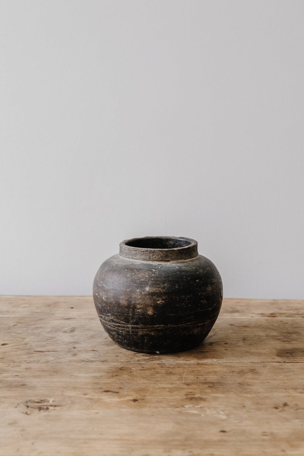 Antique clay pot with weathered patina on wooden surface against plain background