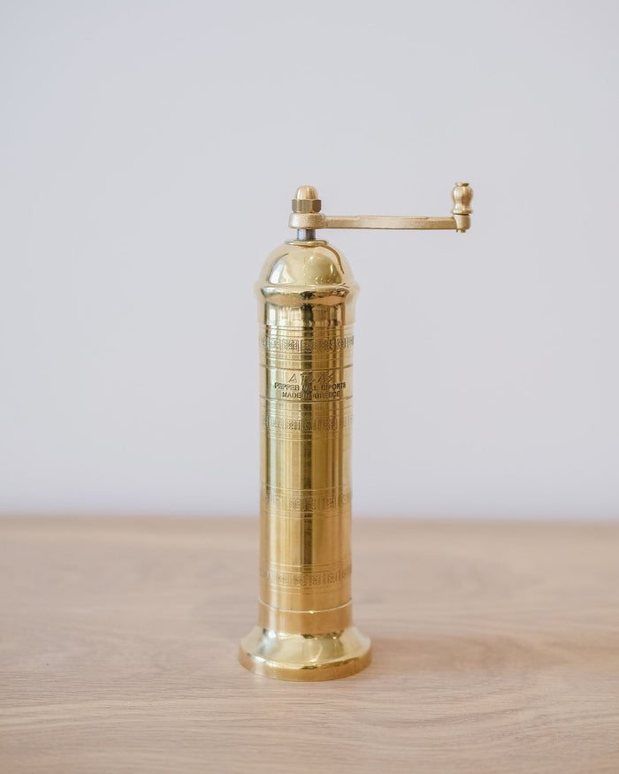 Front view of Atlas Brass Salt Grinder - 8" on an oak table against a white wall.