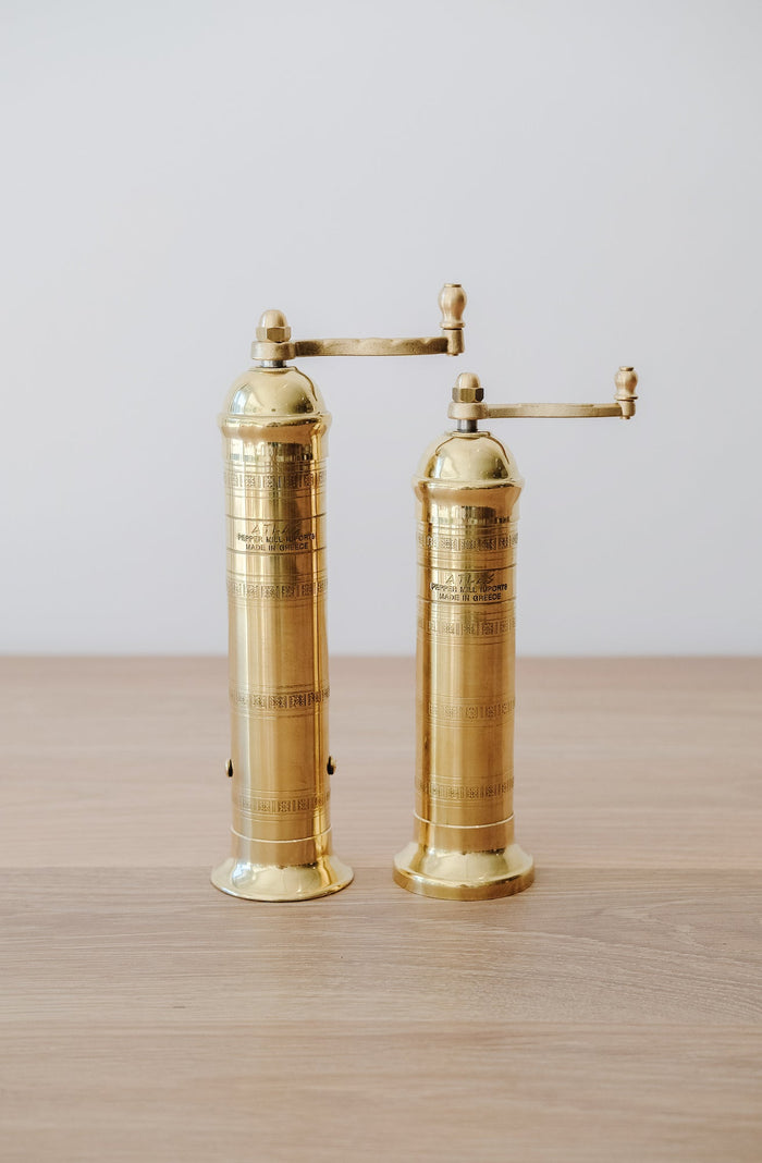Front view of Atlas Brass Salt and Pepper Grinders - 8", 9" on an oak table against a white wall. - Saffron and Poe