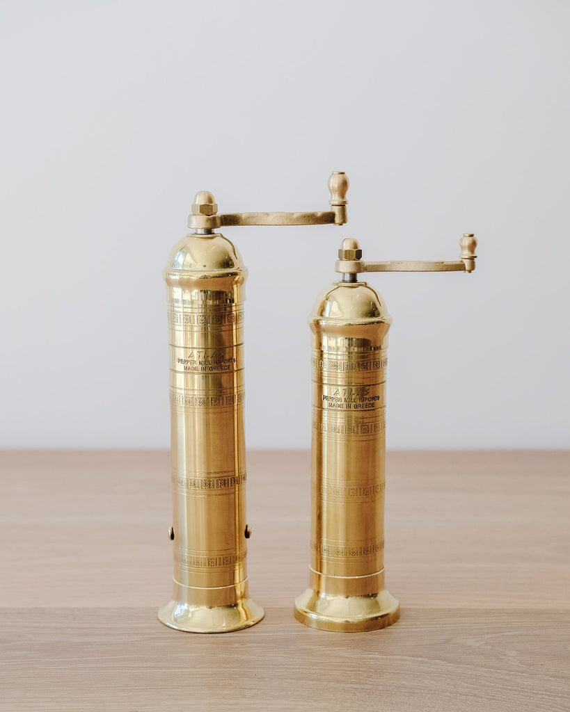 Front view of Atlas Brass Salt and Pepper Grinders - 8", 9" on an oak table against a white wall
