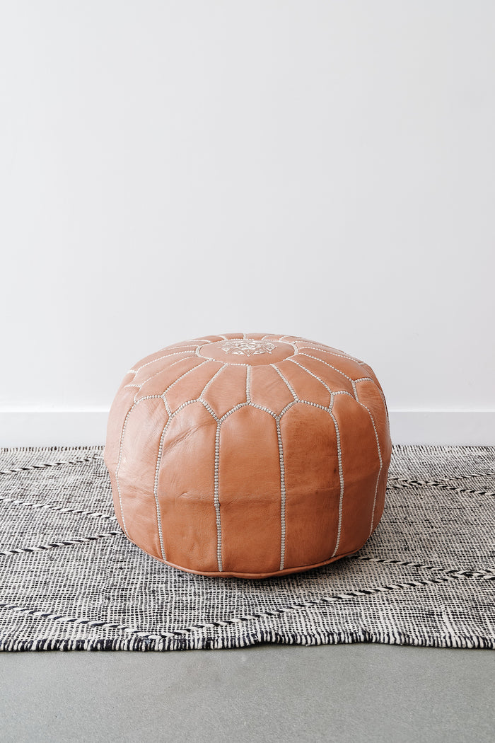 Front view of Embroidered Leather Moroccan Pouf on a Moroccan Kilim Rug against a white wall. - Saffron and Poe