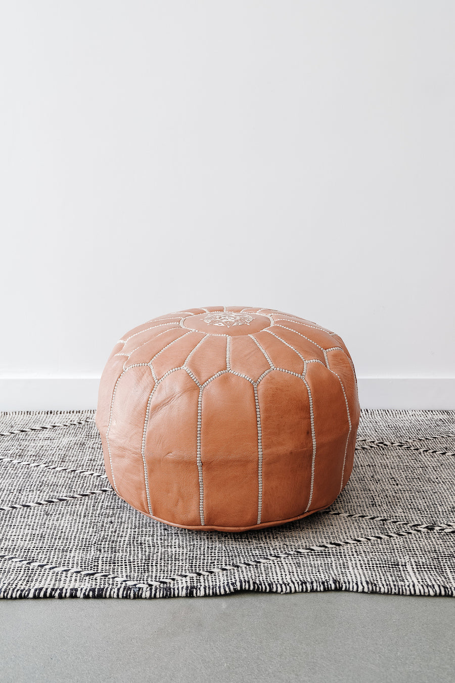 Front view of Embroidered Leather Moroccan Pouf on a Moroccan Kilim Rug against a white wall. - Saffron and Poe