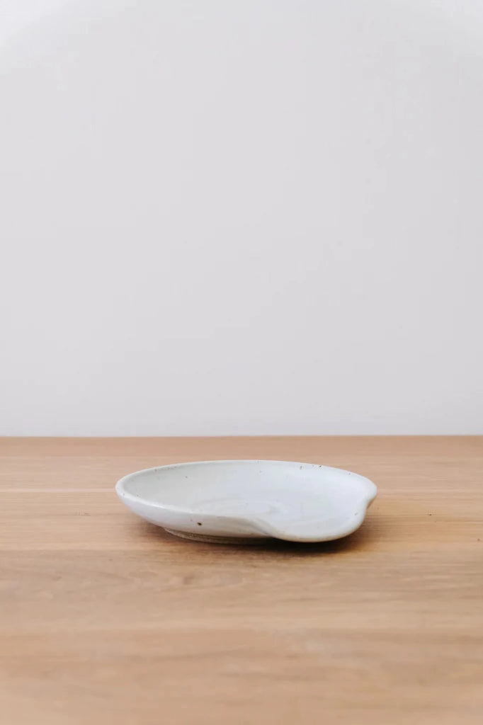 Hand Thrown Ceramic Spoon Rest against white background on an oak table. - Saffron and Poe.