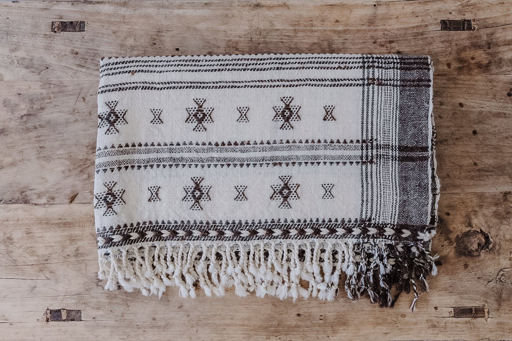 Handwoven Bhujodi bed throw with natural wool and traditional Indian motifs on wooden surface