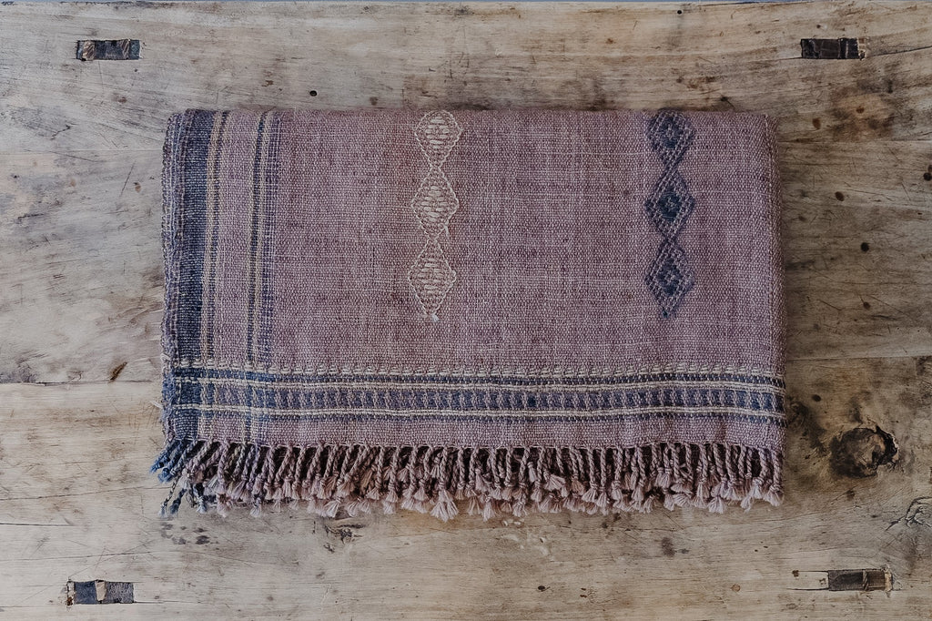 Folded handwoven Bhujodi bed throw in rust with intricate patterns on wooden surface