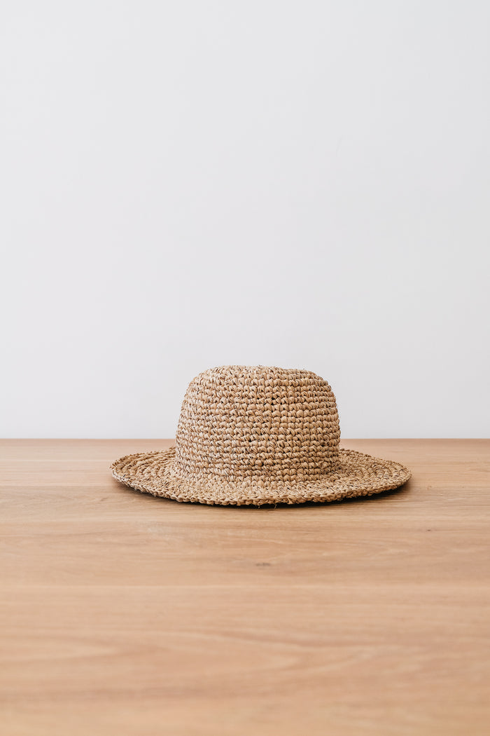 Front view of Handwoven Hat on an Oak Dining Table Against a White Wall. - Saffron and Poe