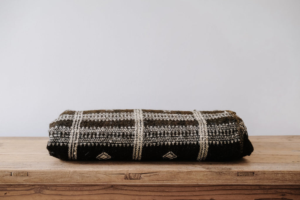 Handwoven Bhujodi blanket dark brown folded on wooden surface with traditional Indian woven patterns