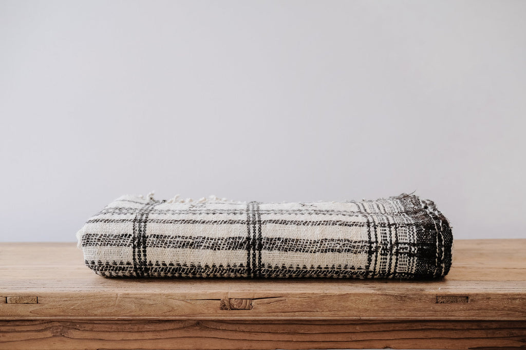 Handwoven Bhujodi Blanket folded with black and natural textured checkered pattern on wooden surface