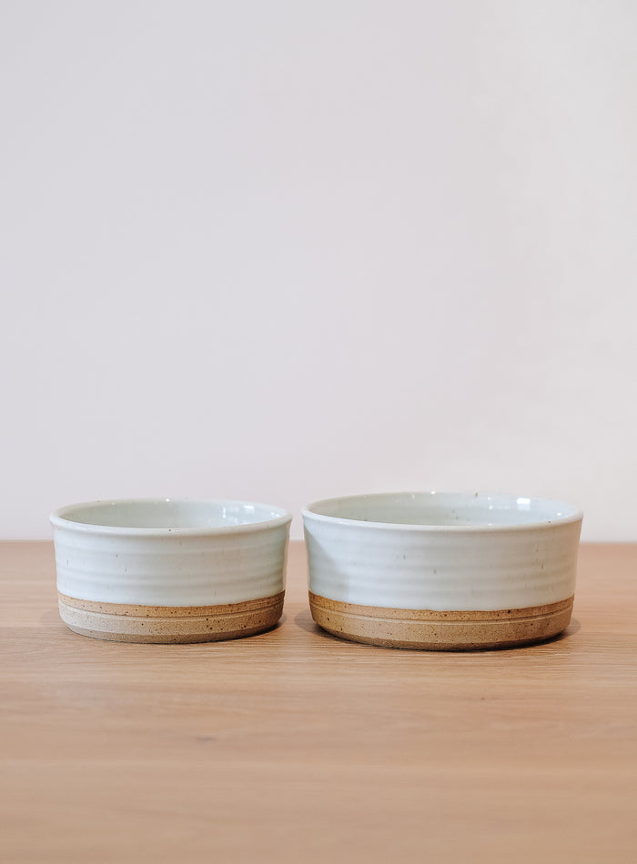 Front view of Hanselmann Ceramic Dog Bowls Nesting Set of 2 on an oak dining table against a white wall. - Saffron and Poe