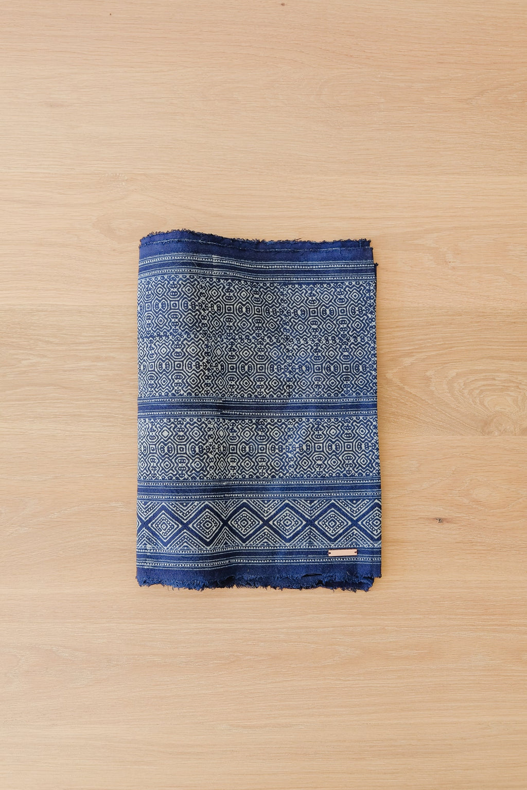 Folded indigo and cream Hmong Batik table runner with intricate traditional patterns on a wooden surface