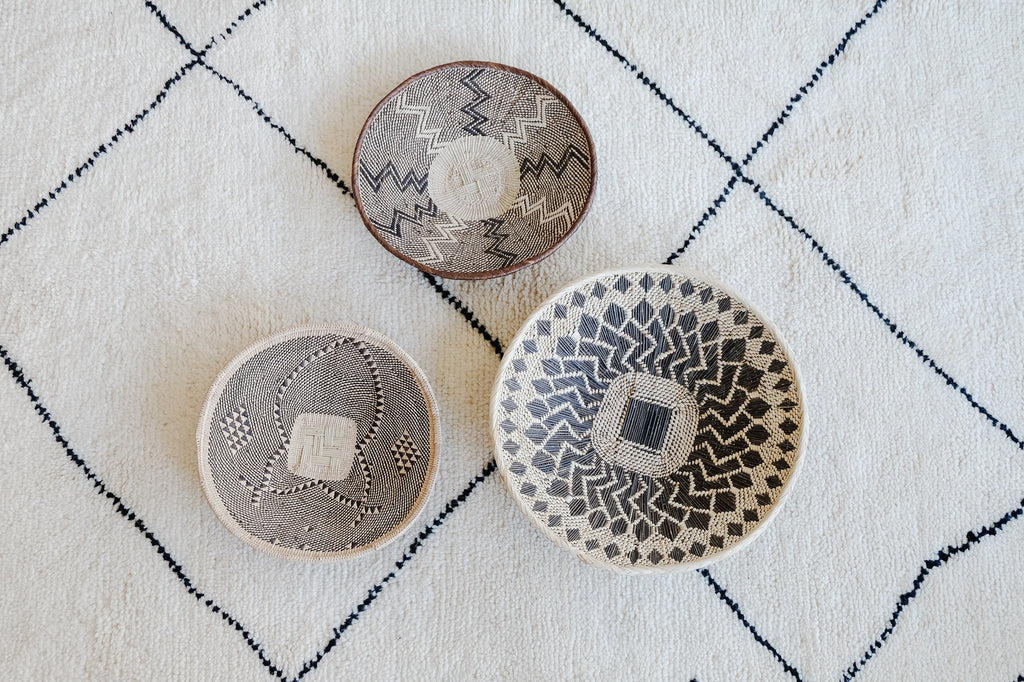 Set of three handwoven Ilala Palm Wall Baskets with traditional patterns in neutral tones on a textured white and black grid background