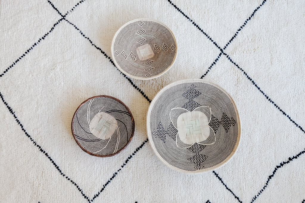 Set of three handwoven Ilala Palm wall baskets with intricate traditional patterns and neutral color palette displayed on a textured white and black rug