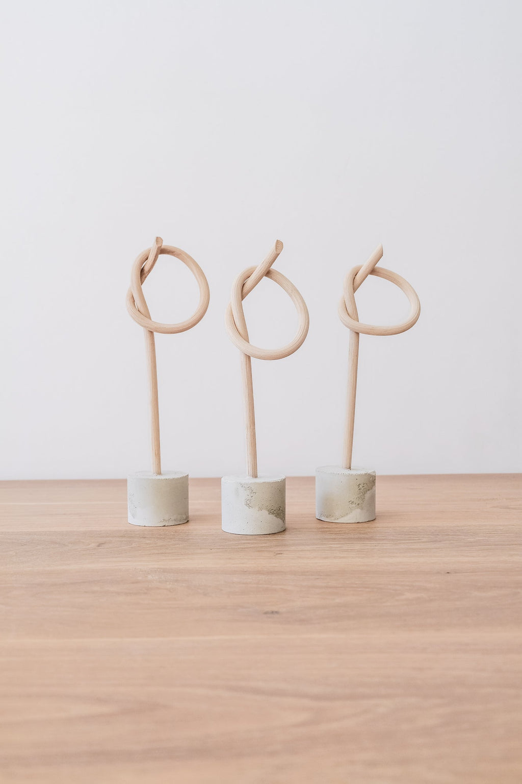 Three wood knot sculptures by Katie Gong on cement bases displayed on a wooden surface against a white background