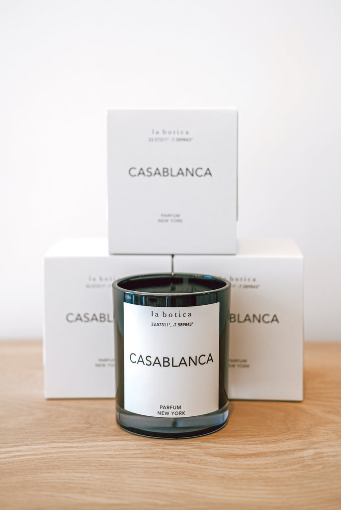 One La Botica Casablanca Candle set in front of three stacked Casablanca Candles against a white background on a oak wood surface - Saffron and Poe