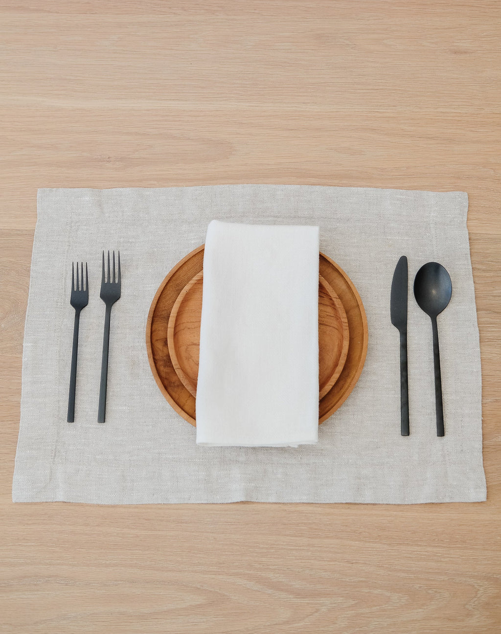 Natural linen placemat with wooden plates, white napkin, and black cutlery on wooden table