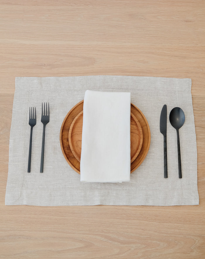 Front view of Natural Linen Placemat with Teak Plates and an Ivory Linen Napkin on a White Oak Dining Table. - Saffron and Poe