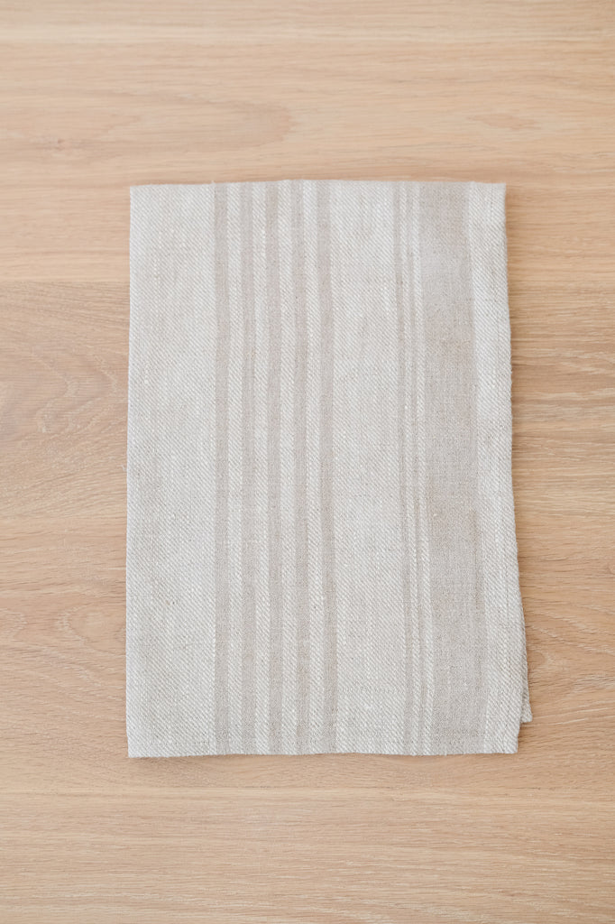 Folded Natural Stripe Linen Hand Towel (Set of 2) on a White Oak Dining Table. - Saffron and Poe