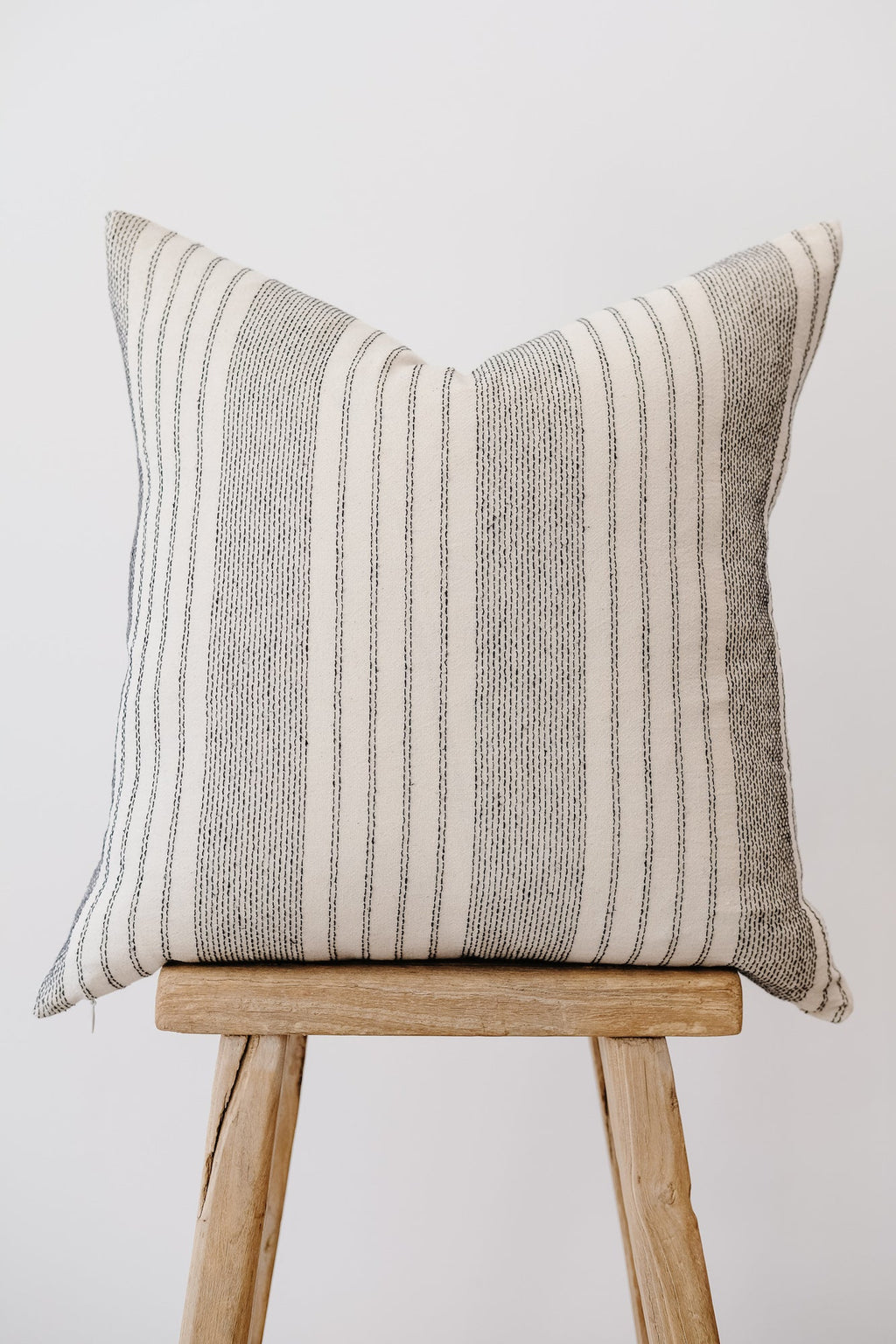 Ivory embroidered pillow with subtle striped pattern on wooden stool