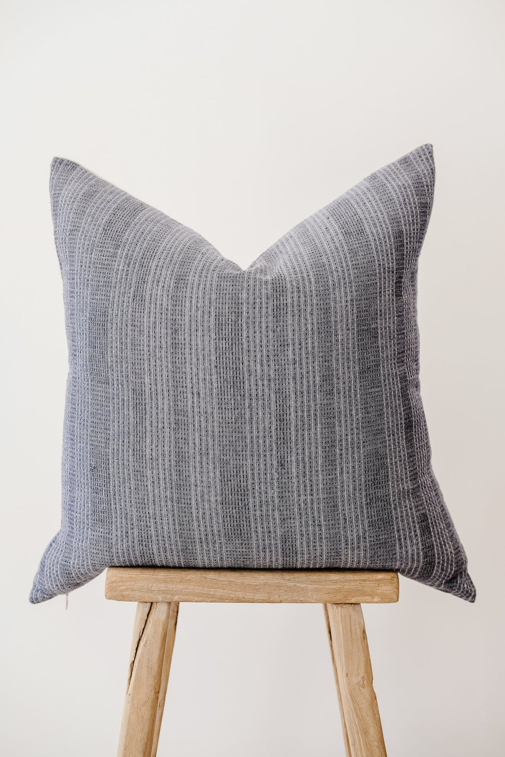 Dusty blue embroidered pillow with subtle textured pattern on wooden stool