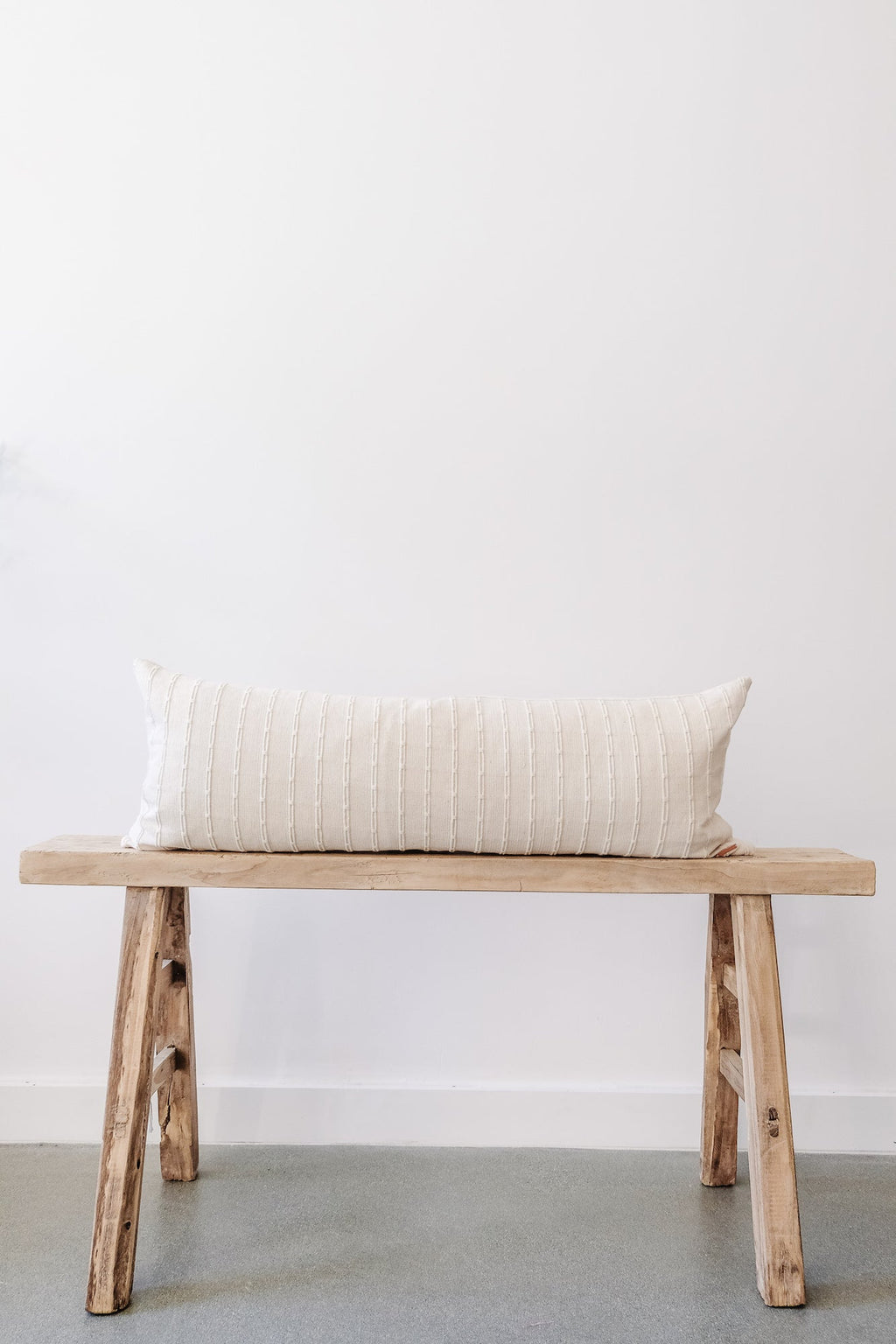 Ivory embroidered extra long lumbar pillow on wooden bench with neutral background
