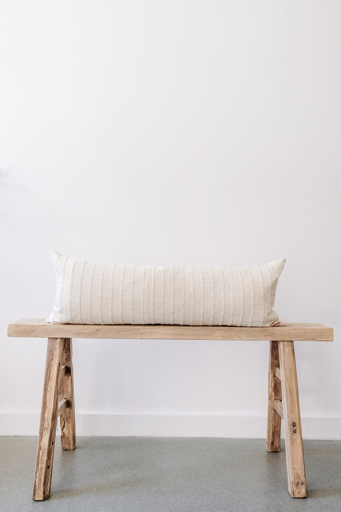 Front view of No. 11 - Hmong Hemp Lumbar Pillow - Extra Long on an Antique Bench against a white wall. - Saffron and Poe