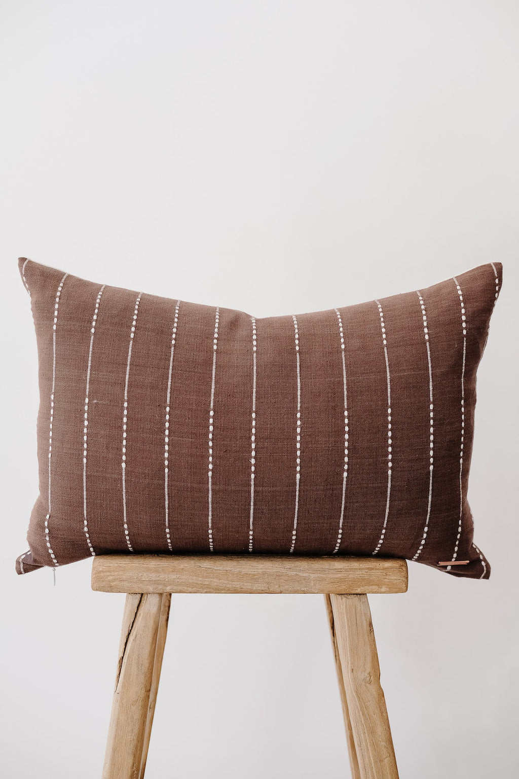 Brown embroidered lumbar pillow with white vertical stitch pattern on wooden stool