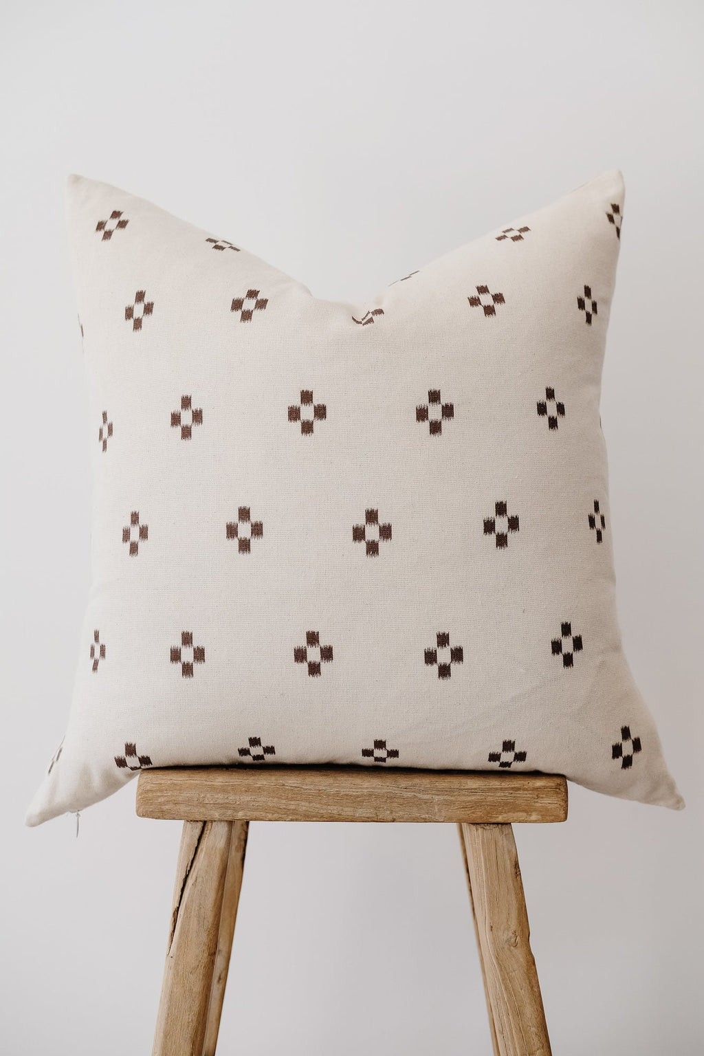 Brown checkered throw pillow with small geometric pattern on wooden stool