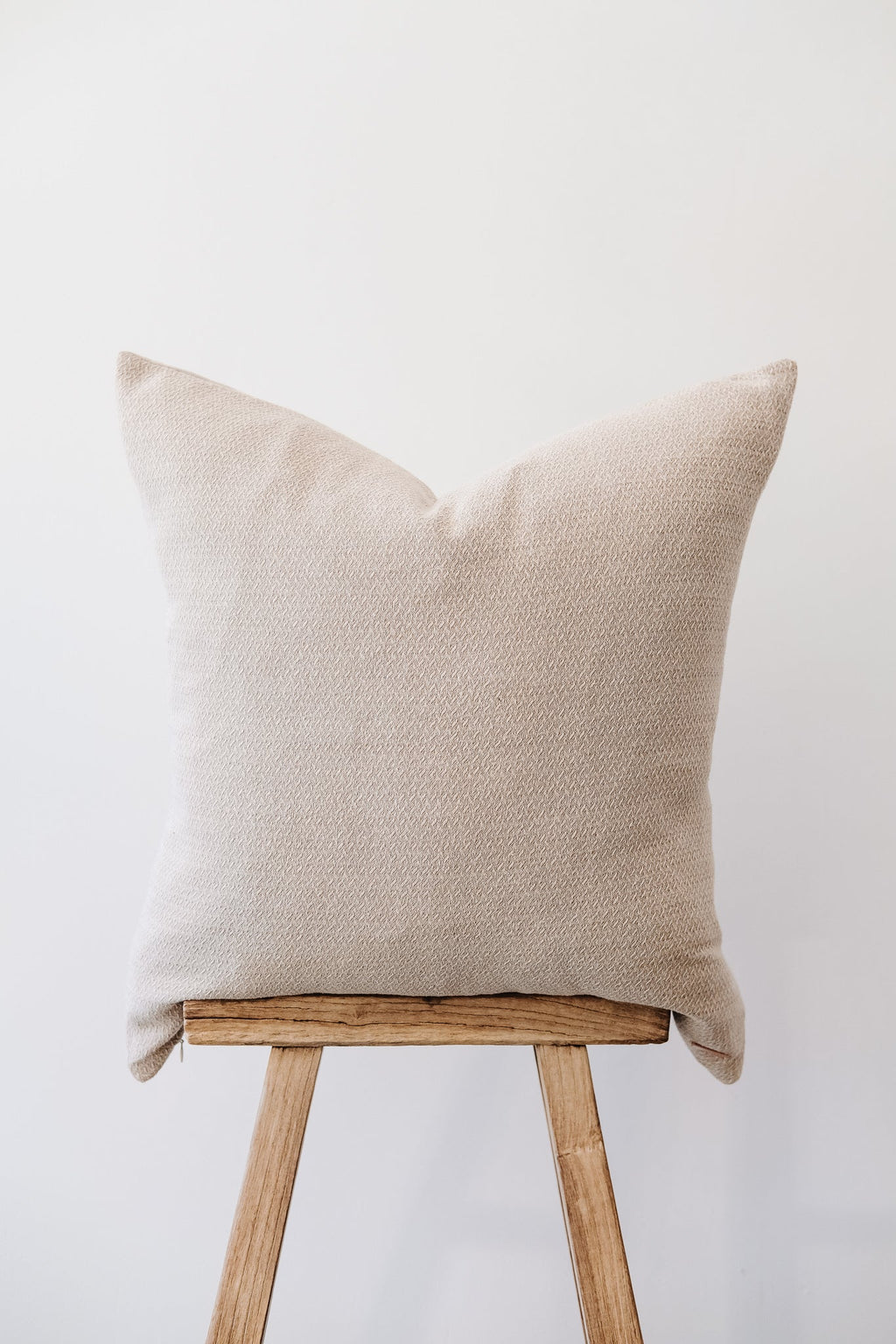 Natural embroidered pillow with subtle texture on wooden stool against white background