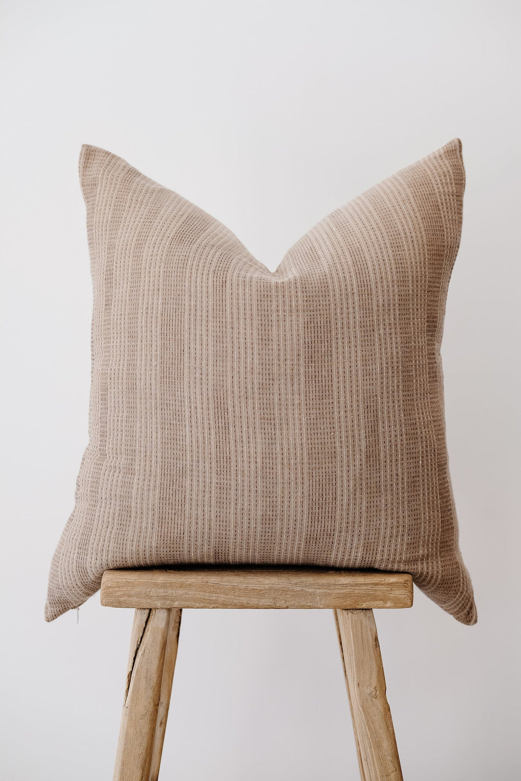 Beige embroidered pillow with subtle textured pattern on wooden stool