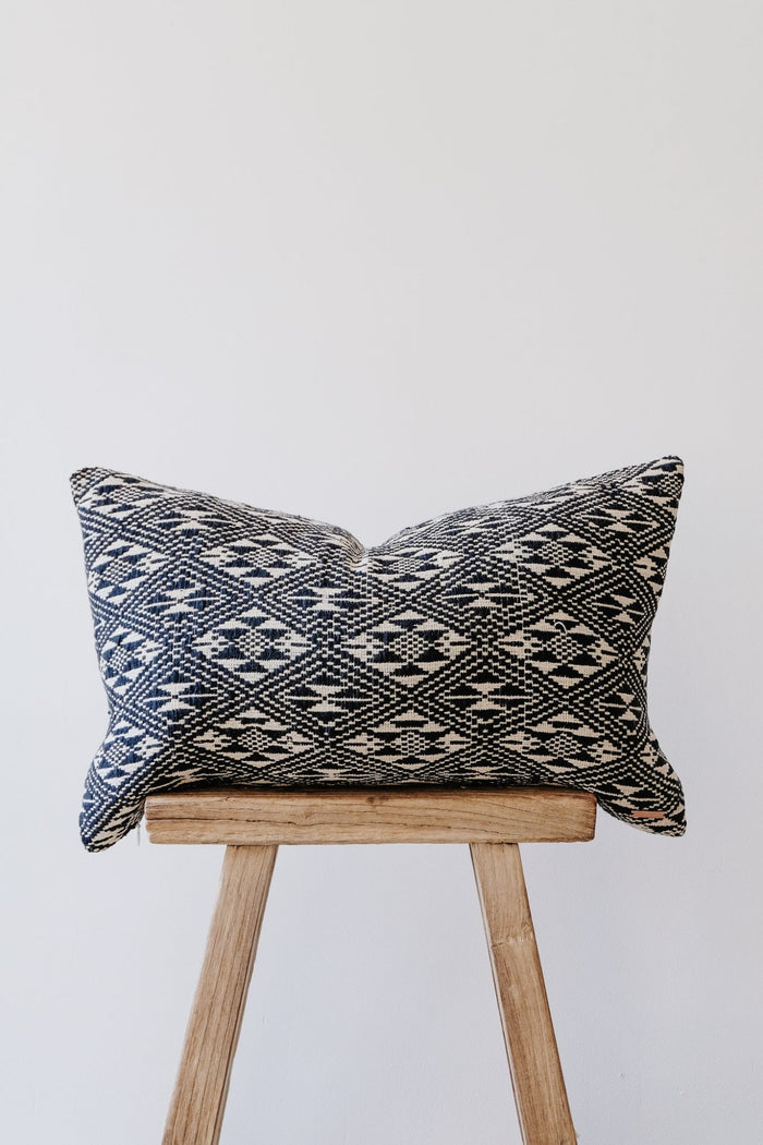 Front view of No. 19 - Antique Miao Lumbar Pillow on an Antique Stool against a white wall. - Saffron and Poe