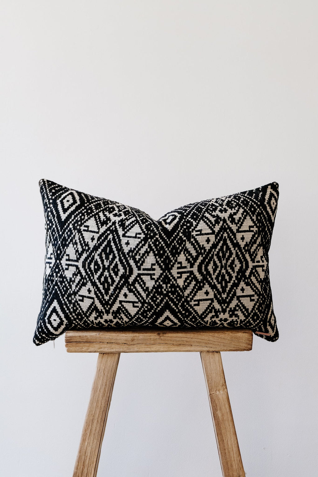 Antique Miao lumbar pillow with black and white traditional geometric patterns on wooden stool against white background
