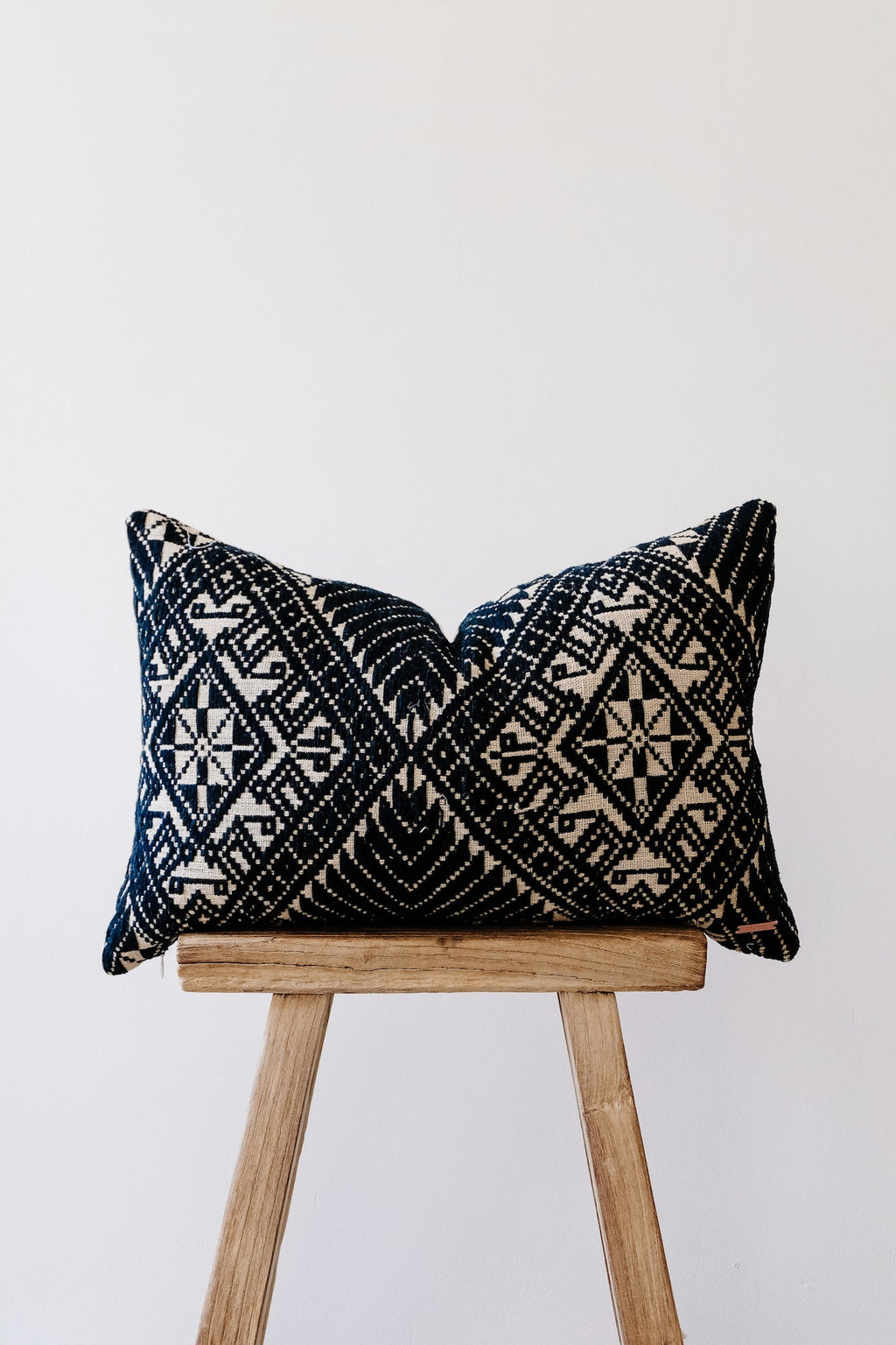 Antique Miao lumbar pillow with intricate black and white traditional woven patterns on wooden stool