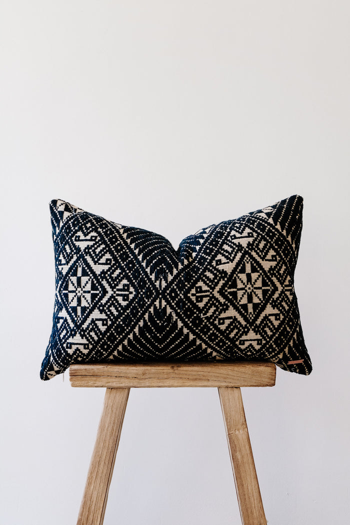 Side view of No.23 - Antique Miao Lumbar Pillow on an Antique Stool against a white wall. - Saffron and Poe
