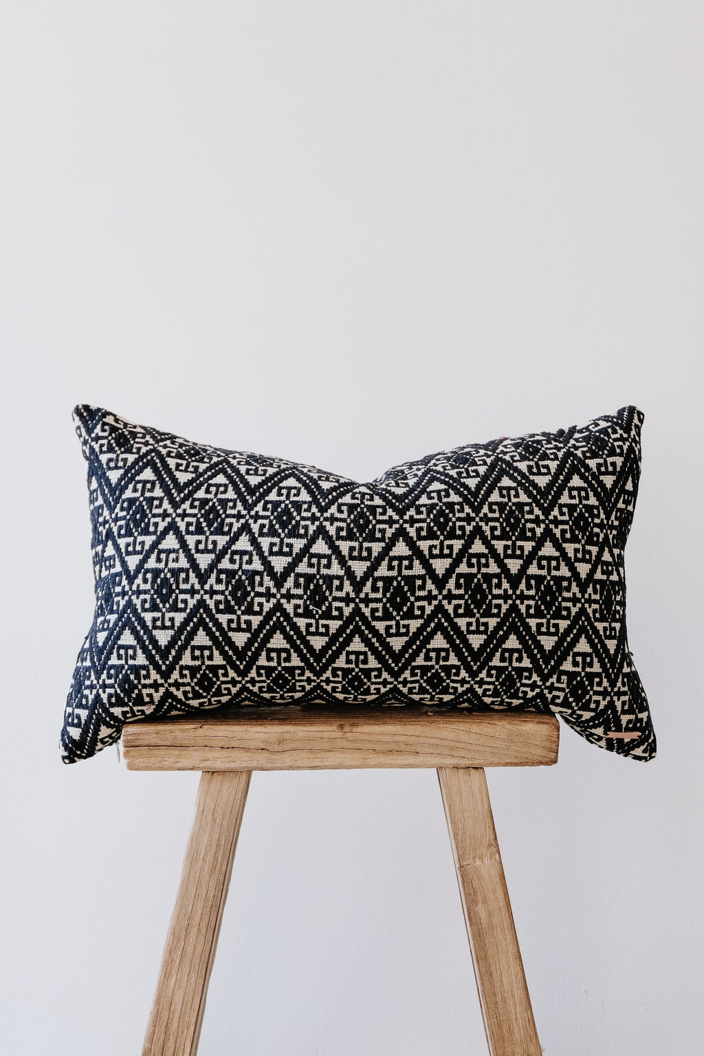 Antique Miao lumbar pillow with intricate black and white geometric patterns on wooden stool